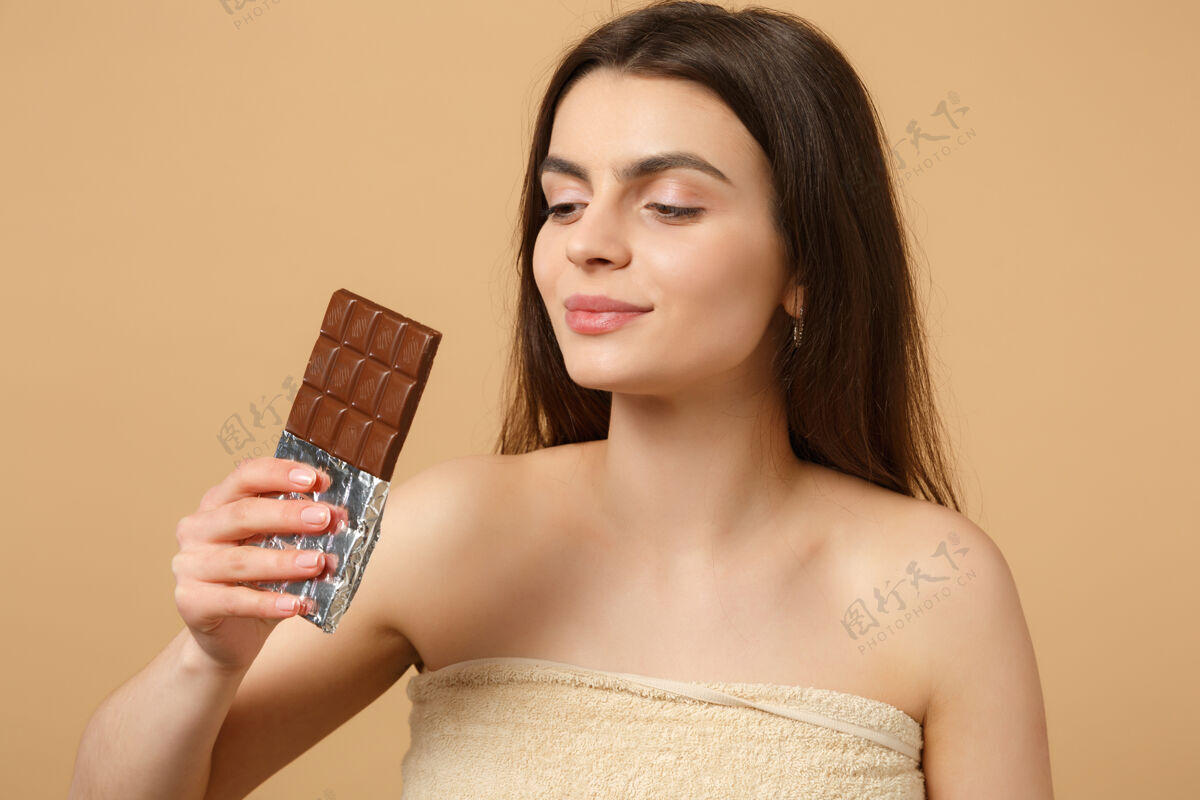 女人近距离拍摄完美肌肤的半裸女人 裸妆将巧克力棒隔离在米色粉彩墙上切片新鲜手