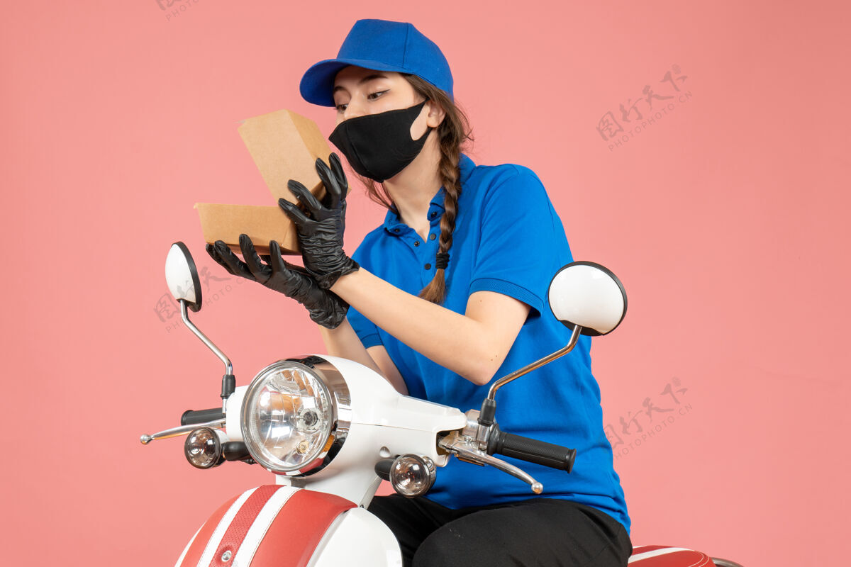 手套俯视年轻专注的女快递员戴着医用口罩和手套打开粉彩桃盒开放人摩托车