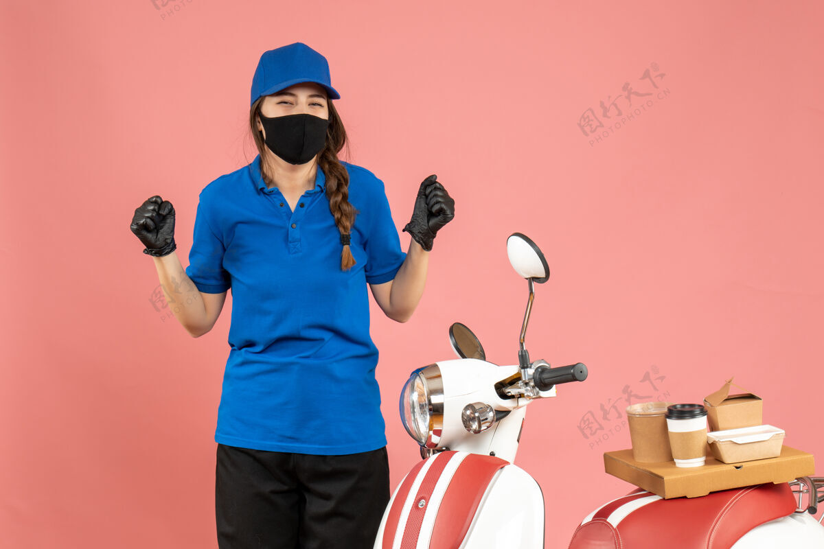 穿俯视图：戴着医用面罩手套的快乐信使女孩站在摩托车旁边 粉色背景上有咖啡蛋糕背景男医疗