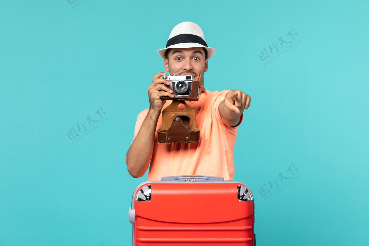 表情带着红色手提箱和蓝色相机拍照的度假男人拍摄照片旅程