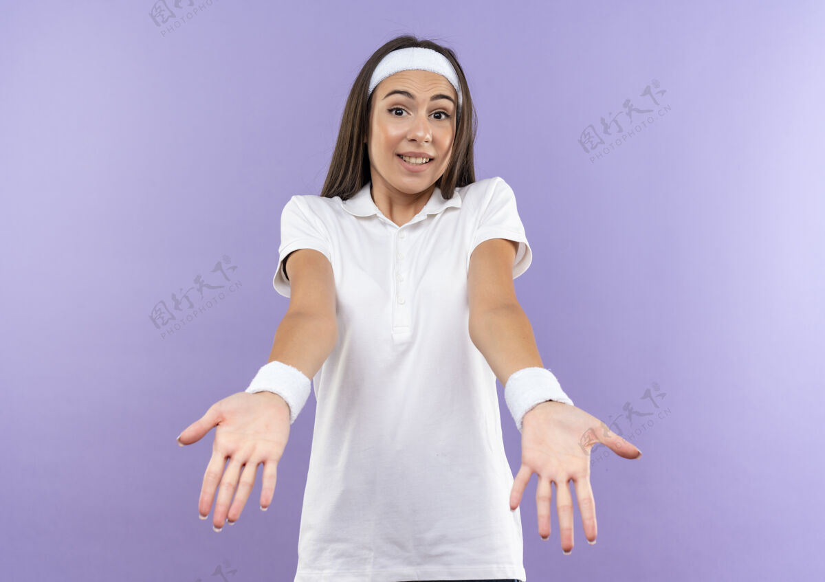 腕带迷茫美丽的运动女孩戴着头带和腕带显示空手孤立在紫色的墙壁上空困惑穿