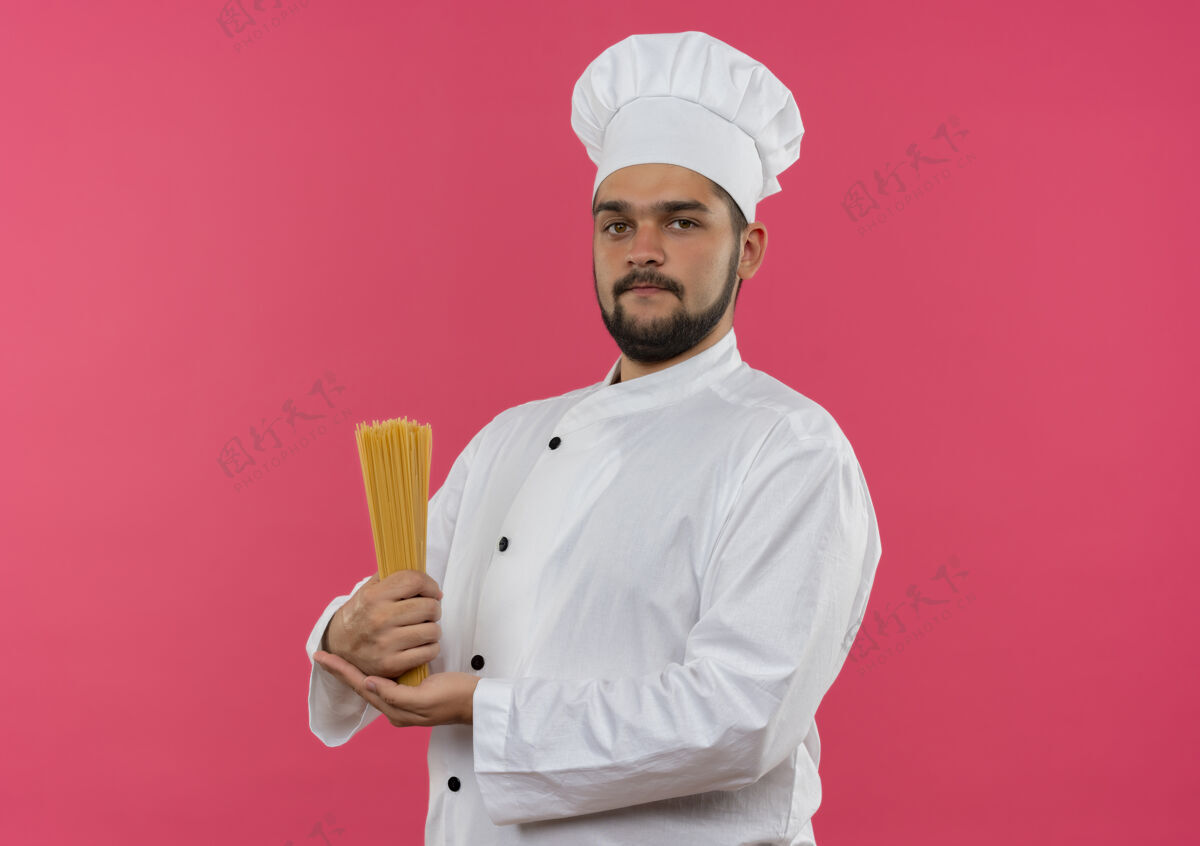 意大利面自信的年轻男性厨师身着厨师制服 手拿意大利面 隔离在粉色墙壁上 留有复制空间厨师制服男性