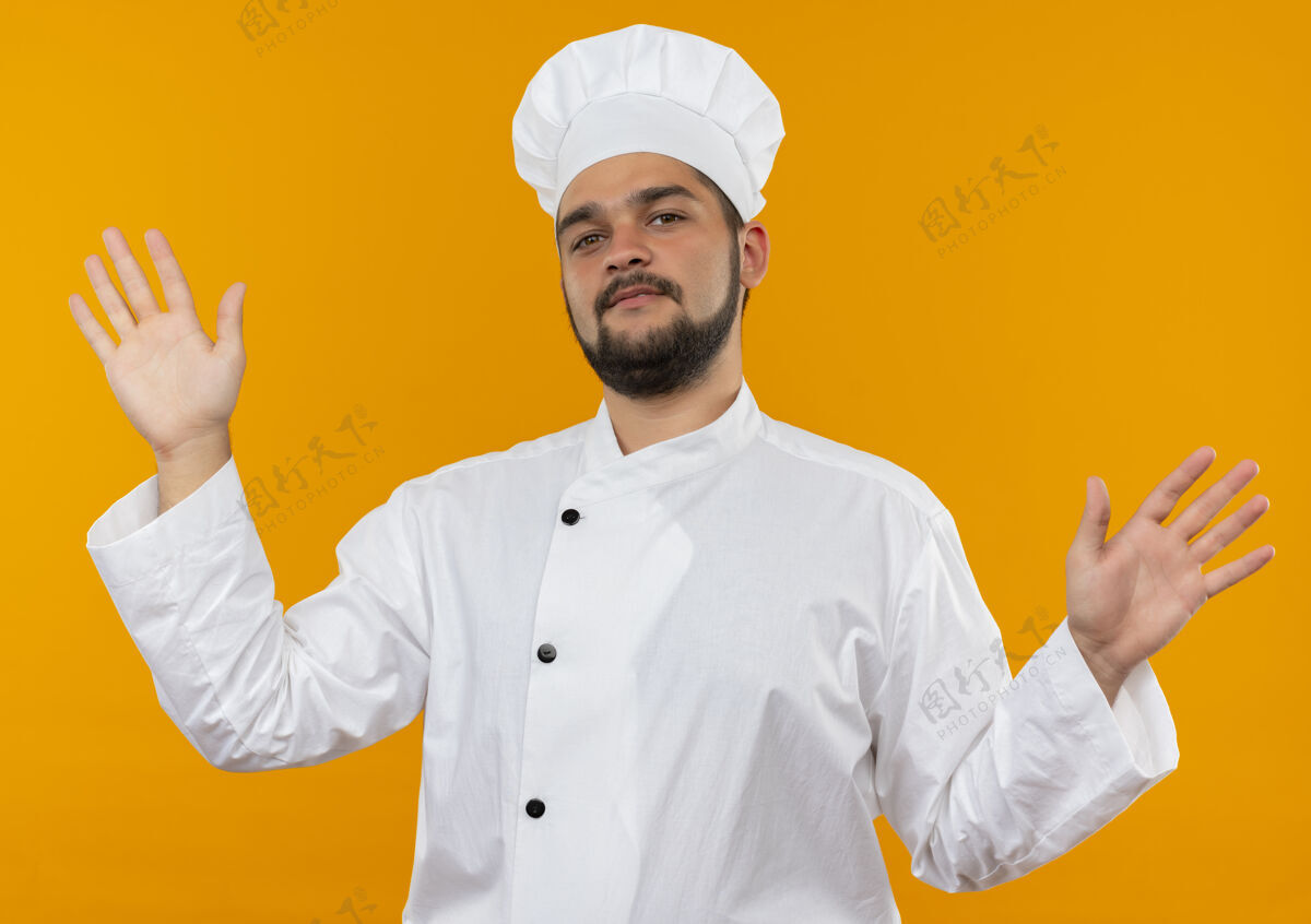 厨师自信的年轻男性厨师身着厨师制服 双手空空地孤零零地站在橙色的墙上手展示自信