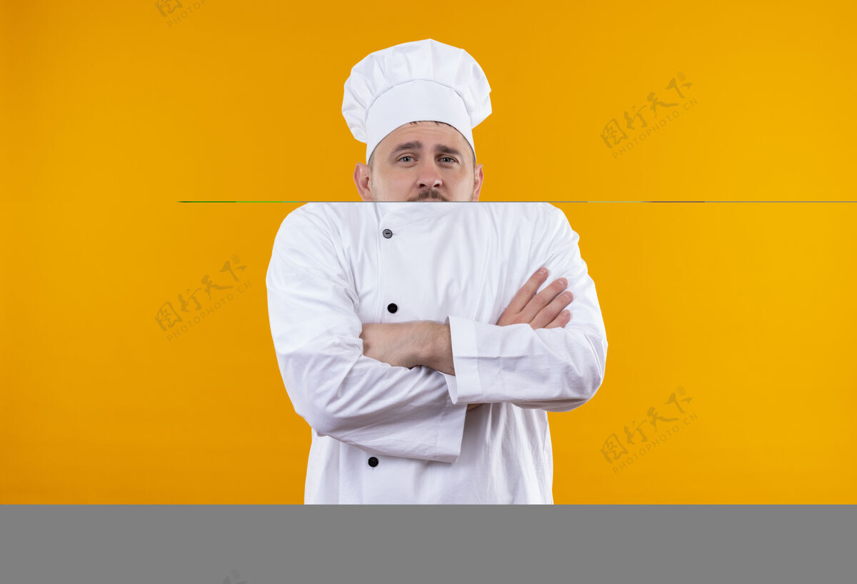 制服自信的年轻帅哥厨师身着厨师制服 以封闭的姿势站在橙色的墙上年轻厨师烹饪