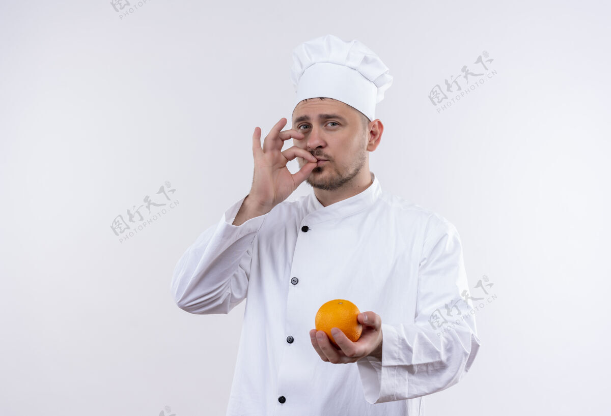 手握自信的年轻帅哥厨师身着厨师制服 手拿橘子 做着美味的手势孤立在白色的墙上厨师年轻自信