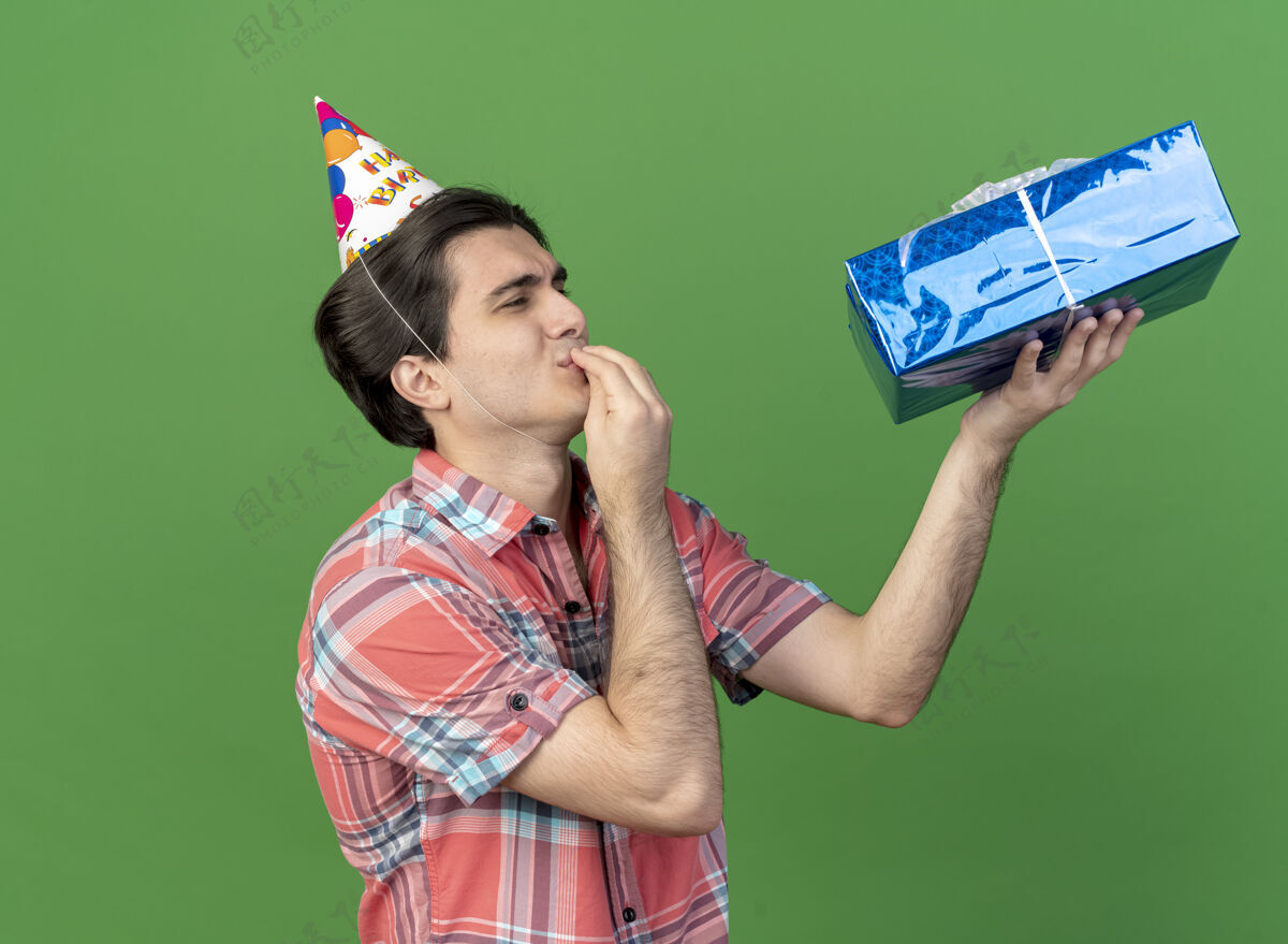 站着兴奋的白种人帅哥戴着生日帽站在一边拿着礼物盒看着美味的标志美味空间拿着