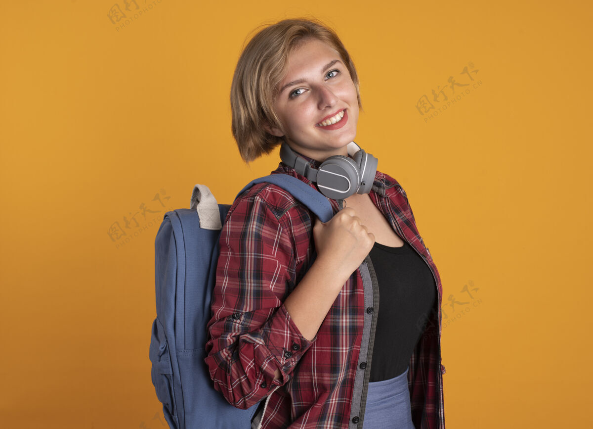 站着微笑着的年轻斯拉夫女学生戴着耳机 背着背包站在一边穿侧着女孩
