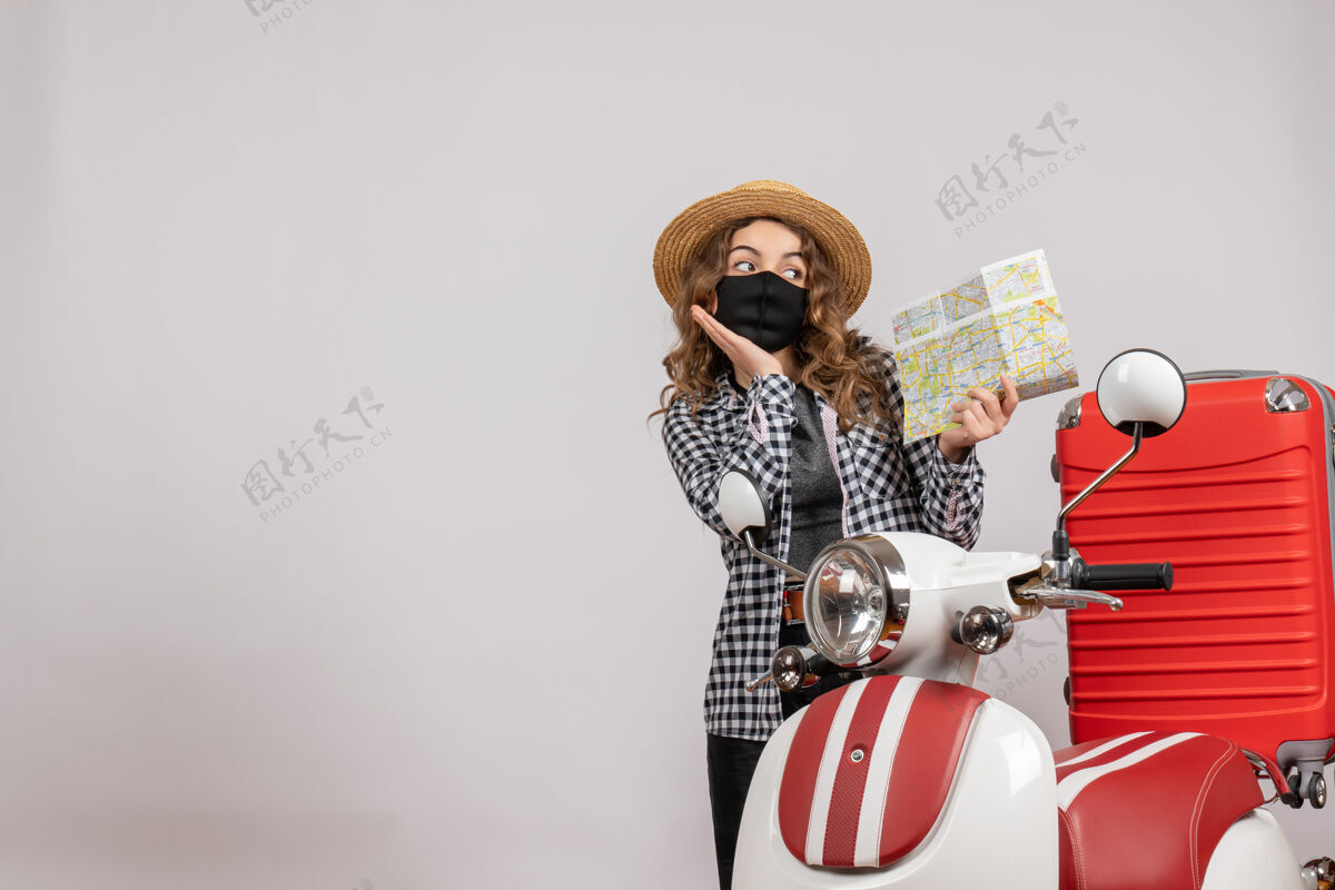 站着戴着面具拿着地图站在摩托车旁边的漂亮女孩手提箱滑板车人