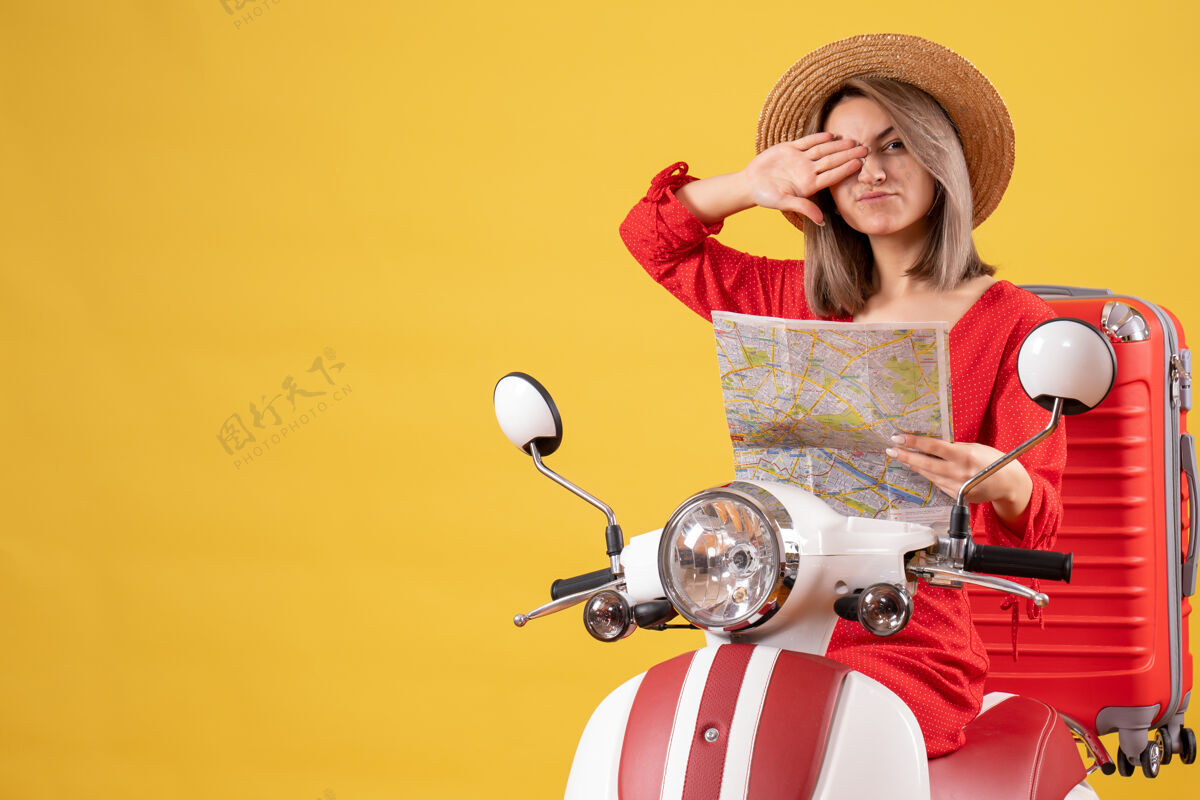 漂亮女孩骑着轻便摩托车的漂亮女孩 手拿着地图 手捂着一只眼睛肖像成人坐着