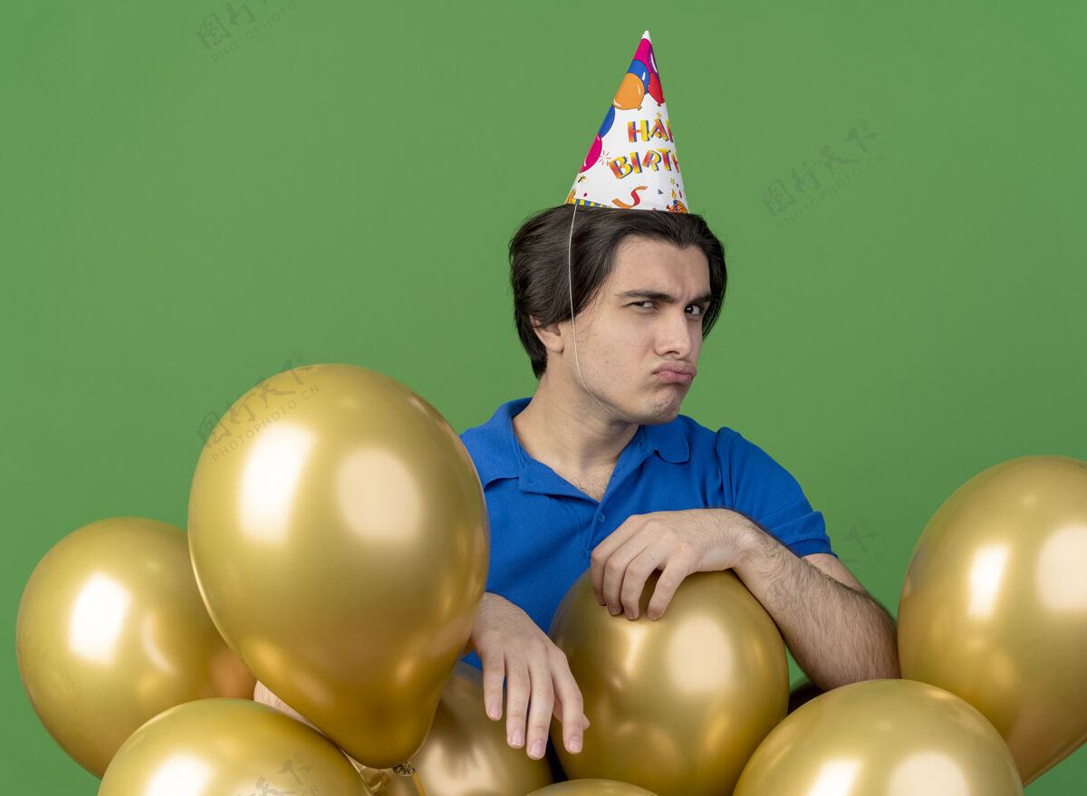 站戴着生日帽的白种人帅哥站在那里拿着氦气球看着相机帽子绿色空间