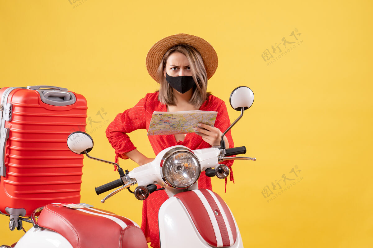 黑色带着黑色面具的紧张的年轻女士拿着地图靠近轻便摩托车地图车辆摩托车