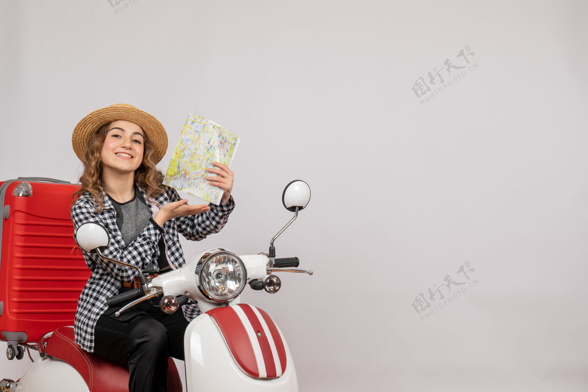 人坐在轻便摩托车上微笑的年轻女子拿着灰色的地图肖像地图车辆