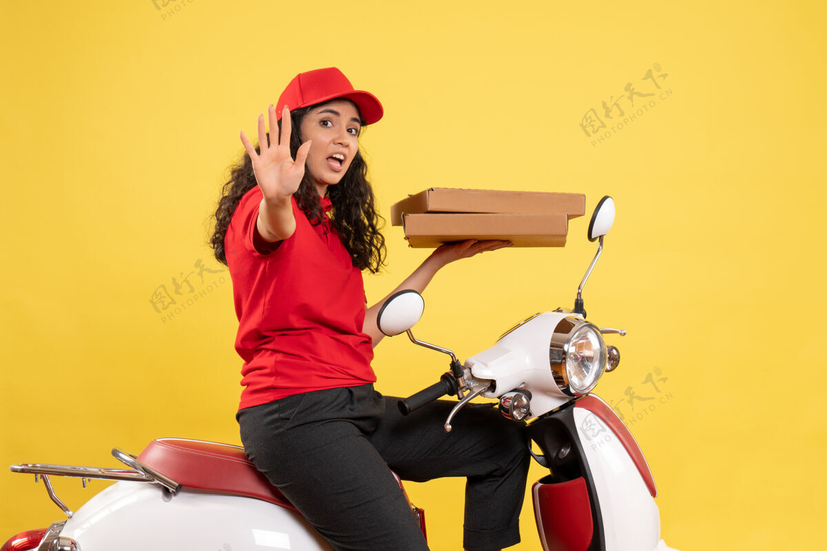 工作正面图骑自行车的女快递员拿着黄色背景的披萨盒工作服女工送货工作拿着送货人