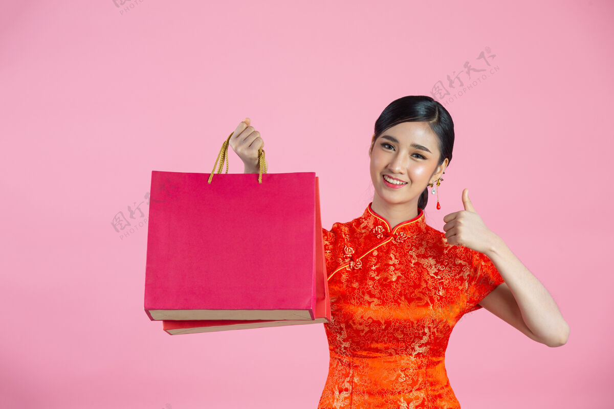 服装美丽的亚洲女人快乐的微笑和购物在中国新年的粉红色背景红色亚洲微笑