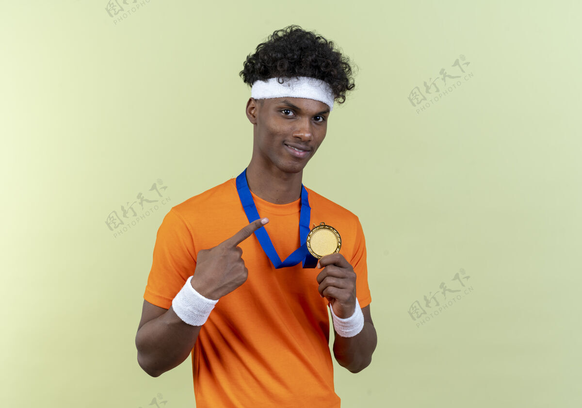 奖牌高兴的年轻黑人美国运动男子戴着头带和腕带举行和点在脖子上的奖牌请头带尖
