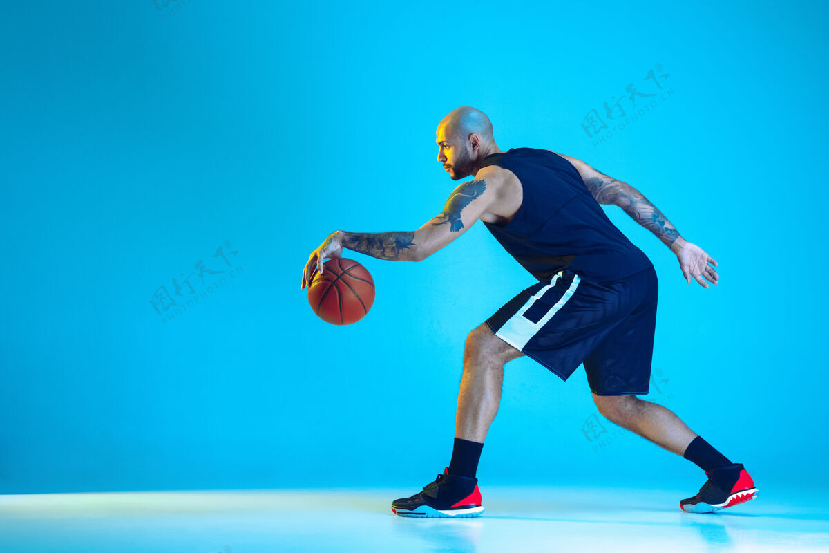 运动员年轻的篮球队员穿着运动服训练 在行动中练习 在霓虹灯下隔离在蓝色的墙上强壮健身冠军