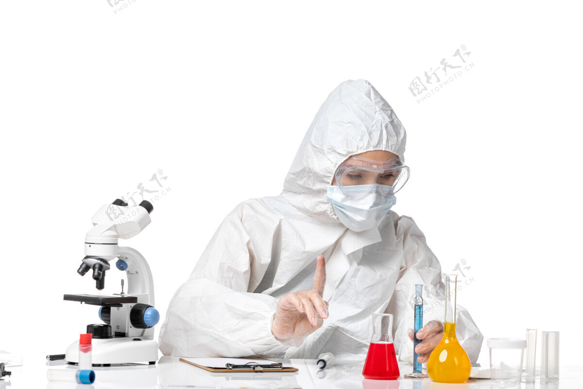 专业人员正面图年轻女医生穿着白色防护服带口罩因柯维德手持蓝色溶液在白色背景上飞溅病毒大流行柯维德-溶液面罩大流行