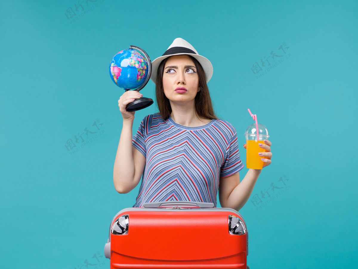 果汁前景度假中的女人手持果汁和地球仪在淡蓝色的背景海上航行度假暑假旅行航行举行人