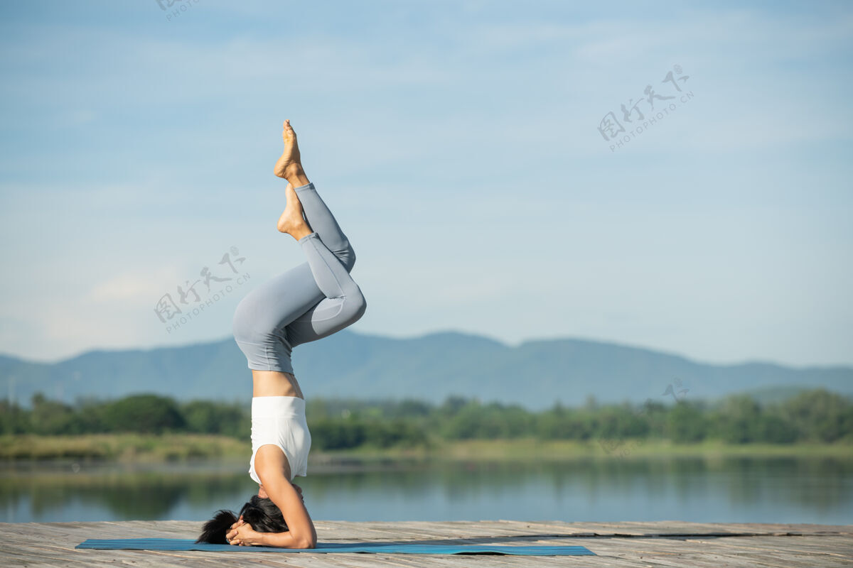 女孩坐在瑜伽垫上在公园里放松的女人年轻的运动型亚洲女人练习瑜伽 做倒立运动 锻炼身体 穿着运动服 裤子和上衣运动人早晨
