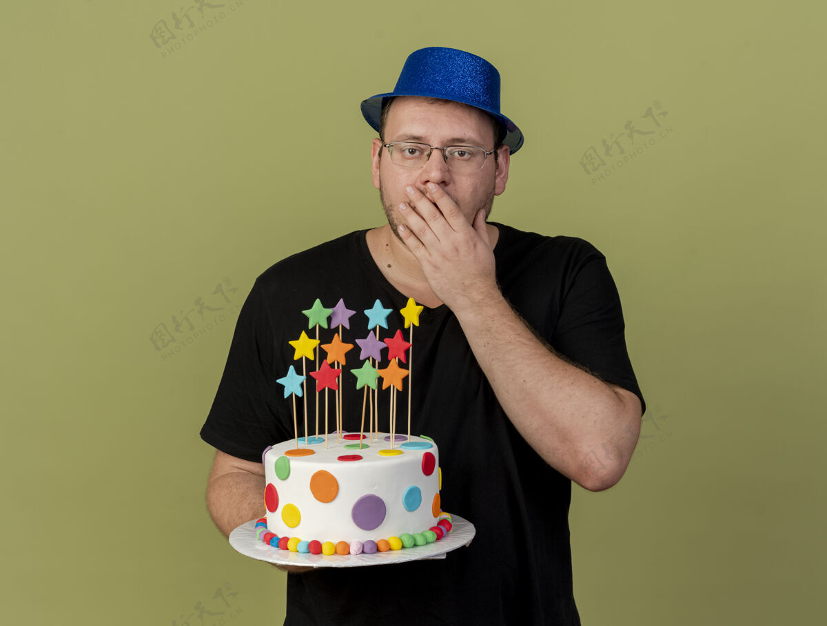 光学震惊的成年斯拉夫人戴着眼镜 戴着蓝色派对帽 手放在嘴上 手里拿着生日蛋糕穿成人橄榄色