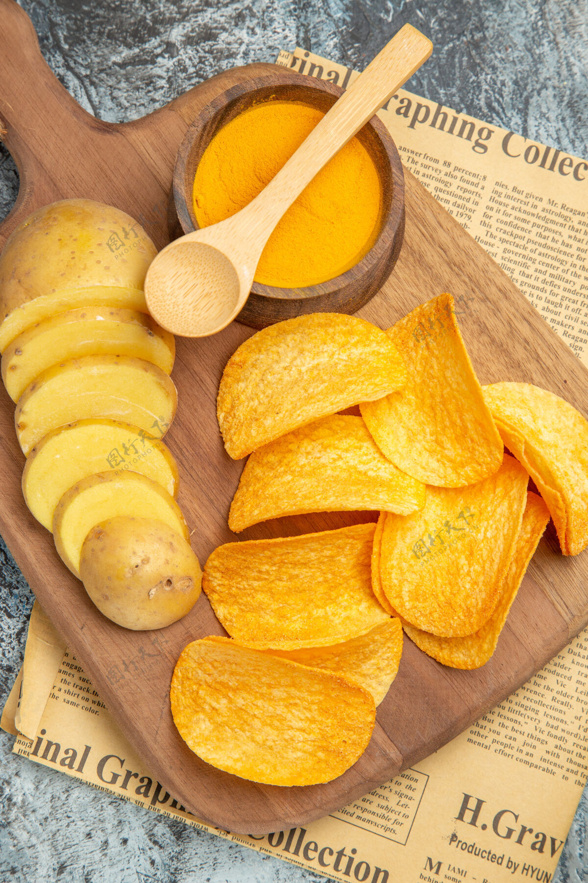土豆美味的自制薯片的垂直视图在灰色背景的报纸上的木制砧板上切土豆片水果蔬菜板