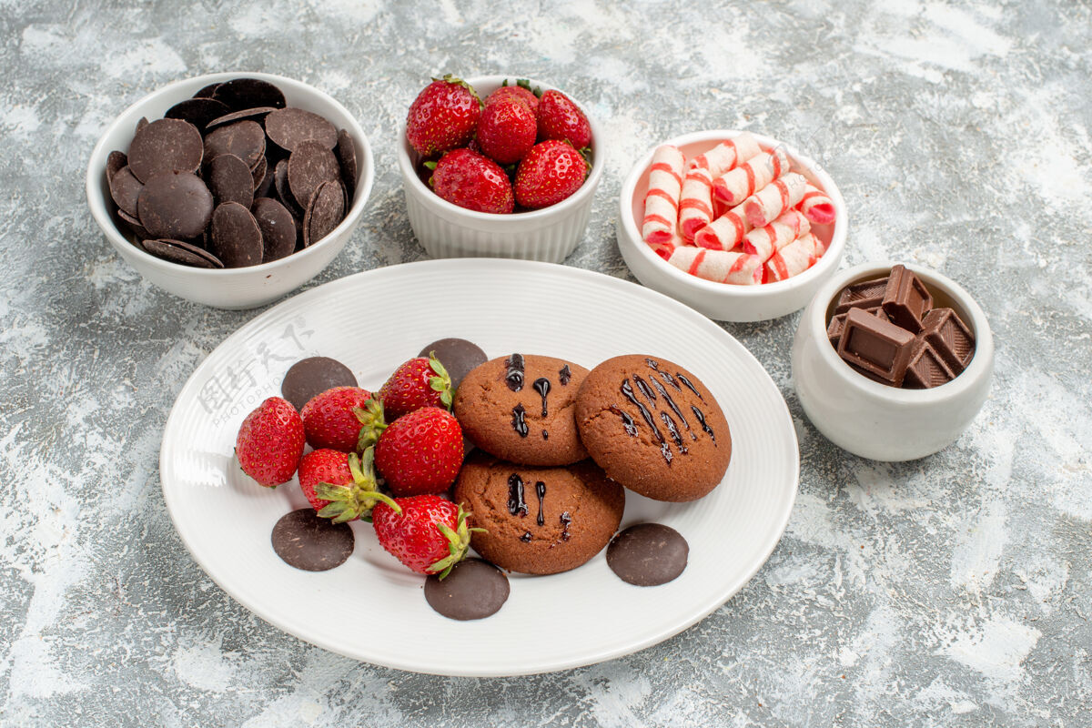 碗底部近距离观看白色椭圆形盘子上的饼干草莓和圆形巧克力 碗周围放着糖果草莓和巧克力 地面上有复印空间水果地面巧克力