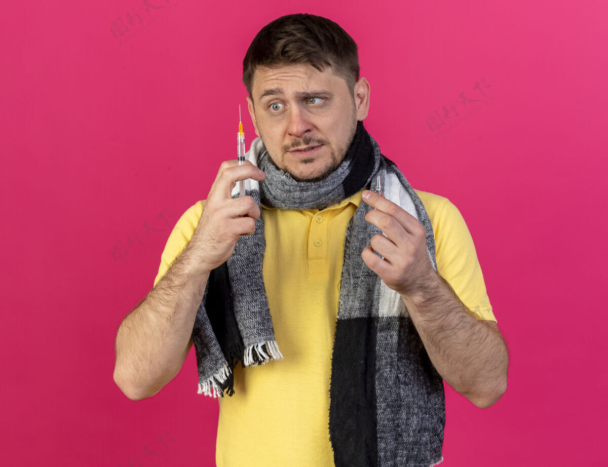 安瓿焦急的年轻金发病斯拉夫男子戴着围巾拿着安瓿 看着粉红色的注射器粉红年轻疾病