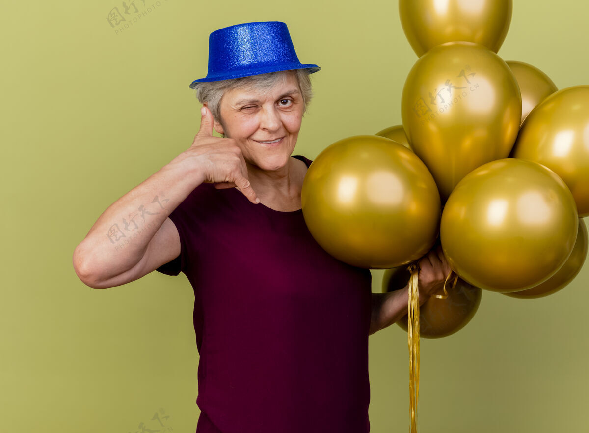老人微笑着戴着派对帽的老妇人站在氦气球旁眨着眼睛橄榄气球帽子