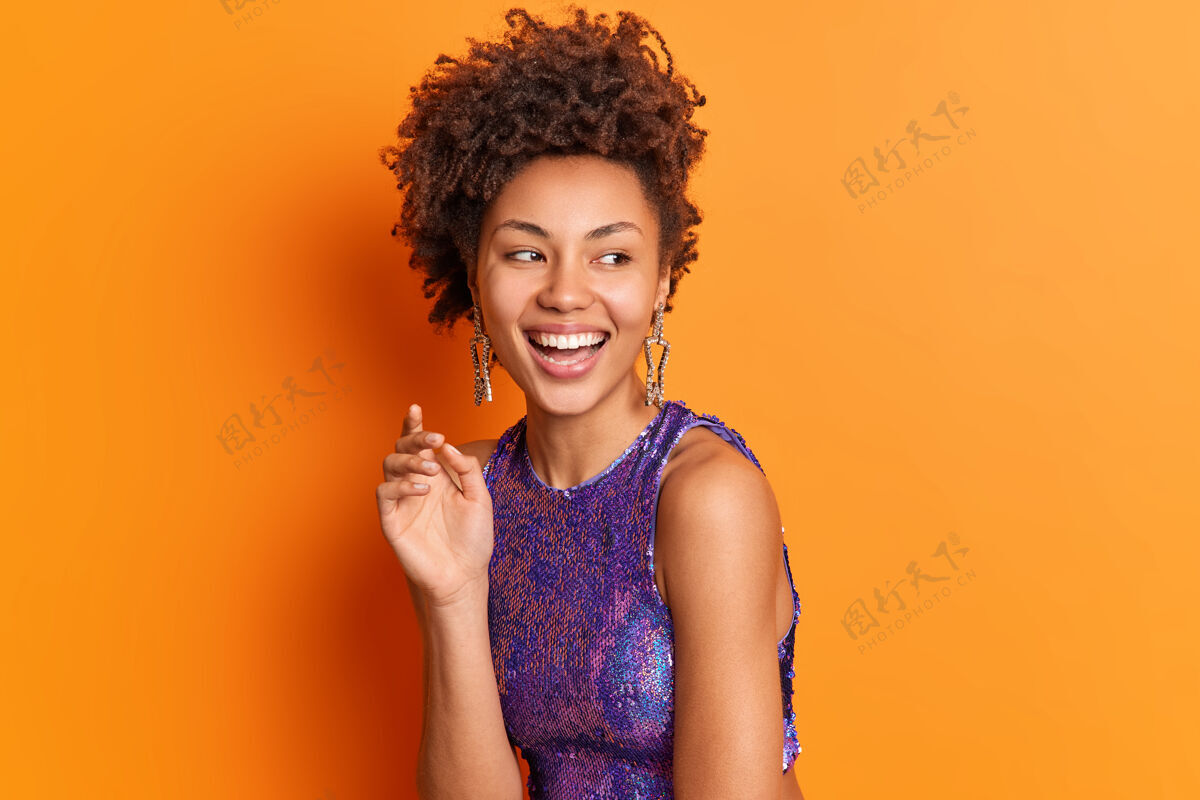 非洲时尚写真的快乐时尚的女人在明亮的衣服耳环微笑广泛地看一边积极孤立的橙色墙壁人牙关快乐