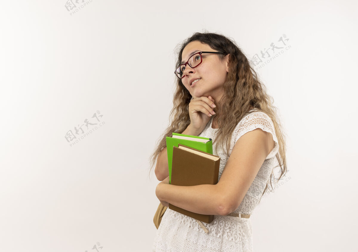衣服体贴的年轻漂亮的女学生戴着眼镜 背着书包 手放在下巴下 看着隔离在白墙上的一面漂亮感情穿