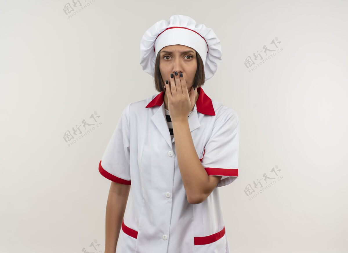 女性惊讶的年轻女厨师穿着厨师制服把手放在嘴上隔离在白墙上烹饪人人