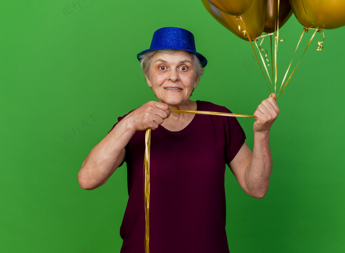 女人戴着派对帽的焦虑的老妇人在草地上拿着氦气球焦虑派对气球