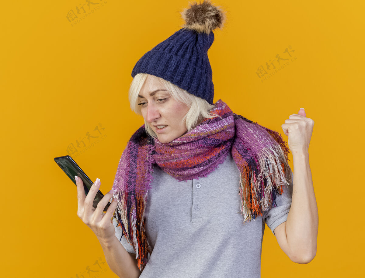 围巾焦急的年轻金发病斯拉夫妇女戴冬季帽子和围巾保持拳头焦虑年轻斯拉夫