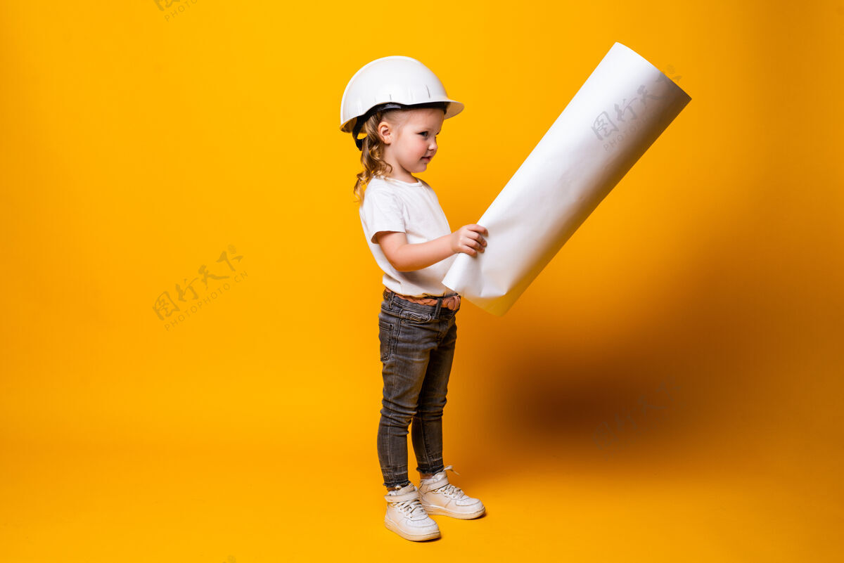 建筑师可爱的小女孩工程师 戴着头盔 把蓝弹簧隔离在黄色的墙上可爱女孩绘画