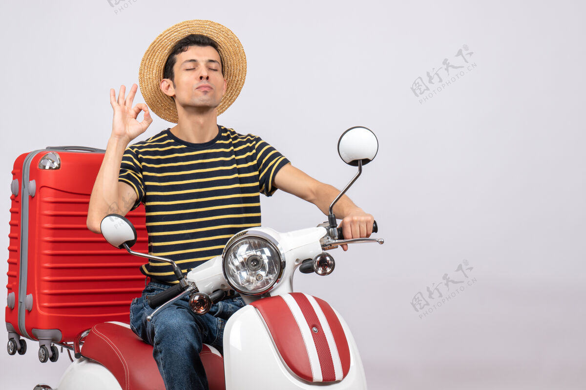 年轻人一个戴着草帽的年轻人坐在轻便摩托车上做着“好”的手势闭上眼睛摩托车传送带关闭