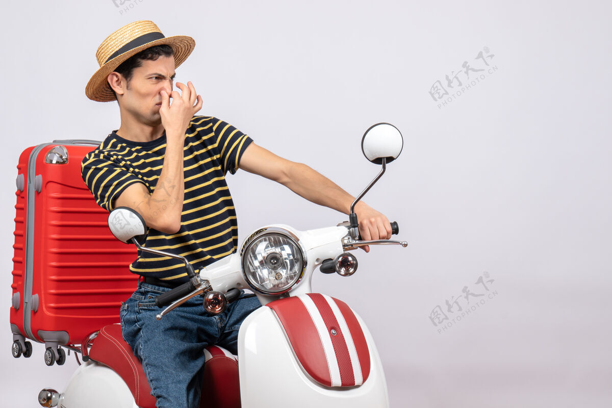 前面一个不高兴的年轻人 戴着草帽 坐在轻便摩托车上 抱着鼻子帽子成人人