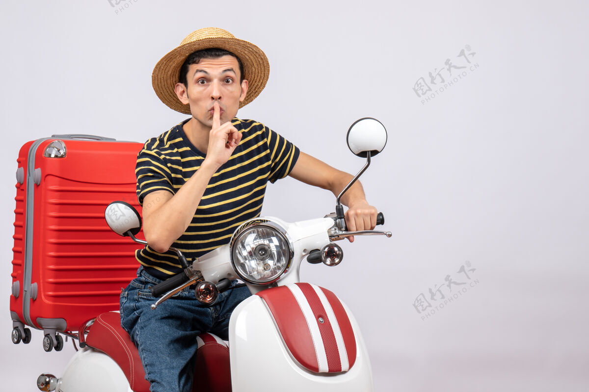 坐着骑着轻便摩托车戴着草帽的年轻人的正视图 正在做安静的标志前面成人视图