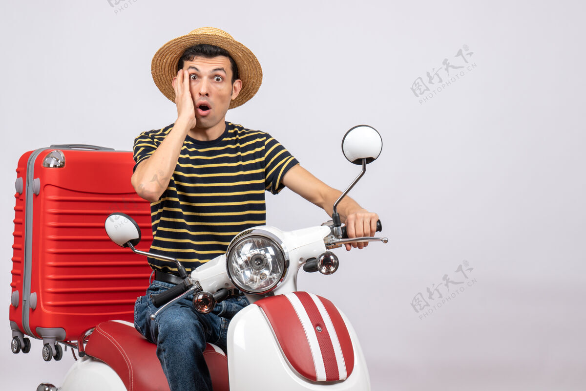 摩托车一个戴着草帽的年轻人坐在轻便摩托车上看着镜头帽子惊讶的年轻人男人