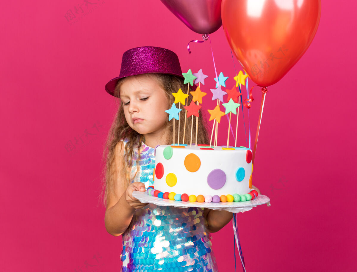 失望失望的金发小女孩 戴着紫色派对帽 手里拿着氦气球 看着粉色墙上孤立的生日蛋糕 还有复制空间帽子氦小
