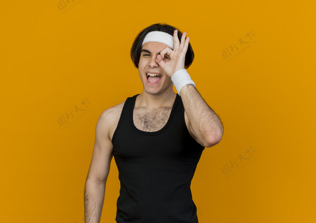 运动装身穿运动服 头戴头巾的年轻人微笑着唱得很好 透过橘色墙上的这个标志看Ok感觉人