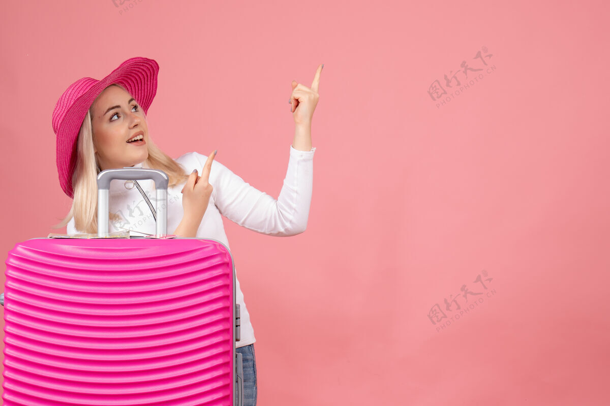 快乐正面图：年轻女士站在粉色手提箱后面 手指向上小姐欢呼前面