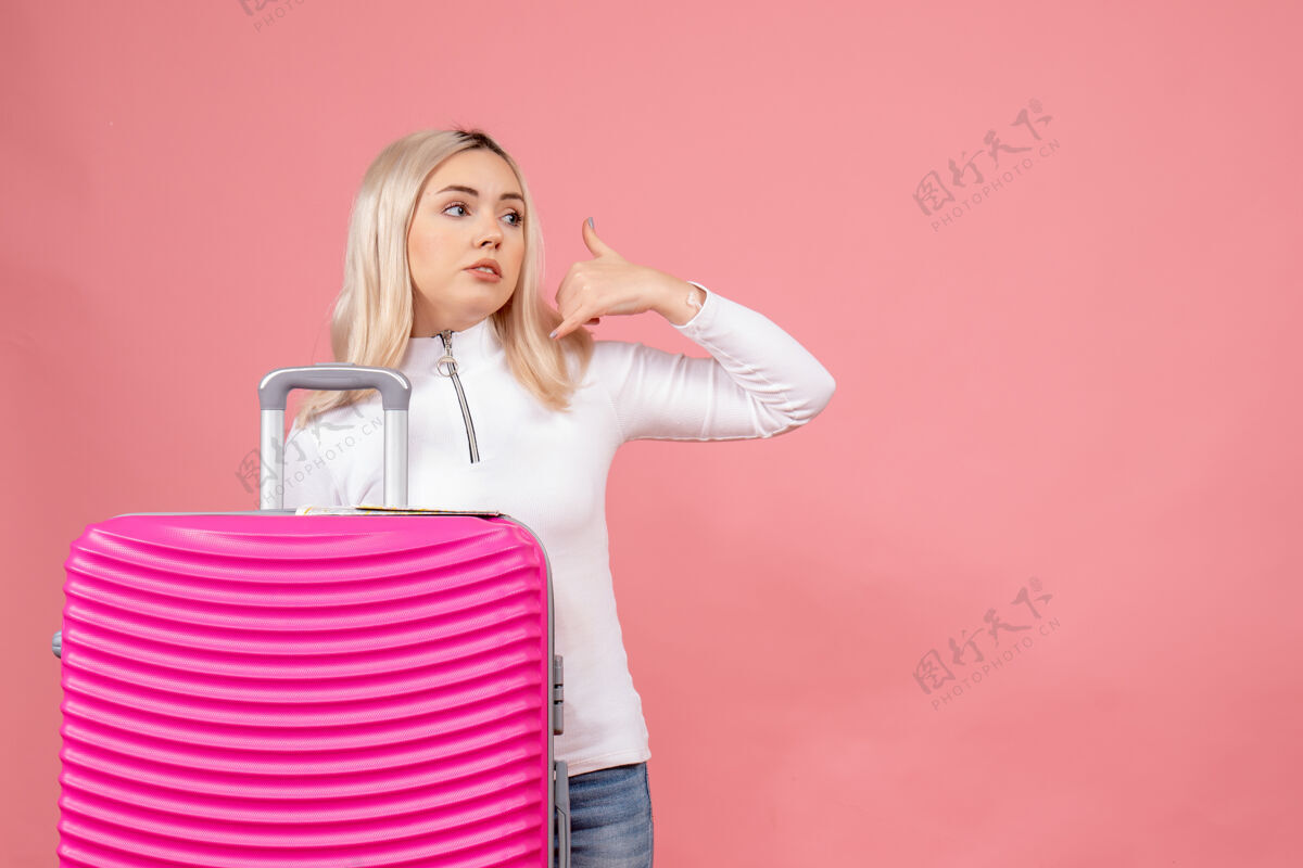 年轻女士正面图：年轻女士站在粉色手提箱后面打电话给我视图制造模型
