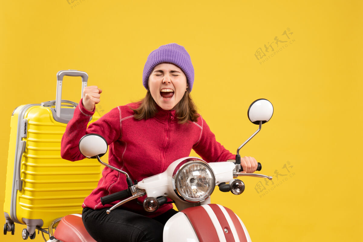 摩托车前视图：骑着轻便摩托车的小女孩带着黄色手提箱尖叫着尖叫前面年轻女孩