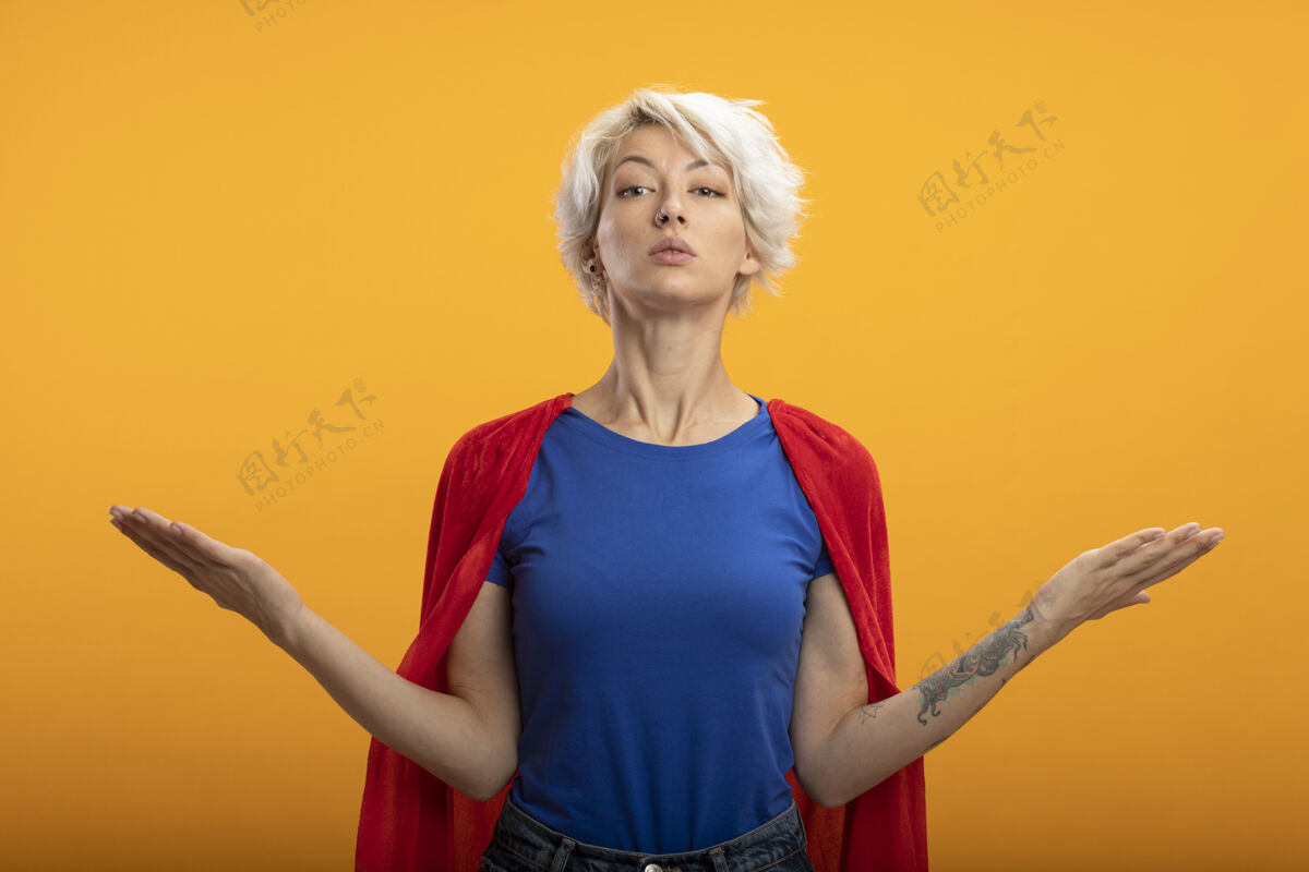女人身着红色斗篷的自信女超人在橙色的墙上张开双手脸超级英雄人
