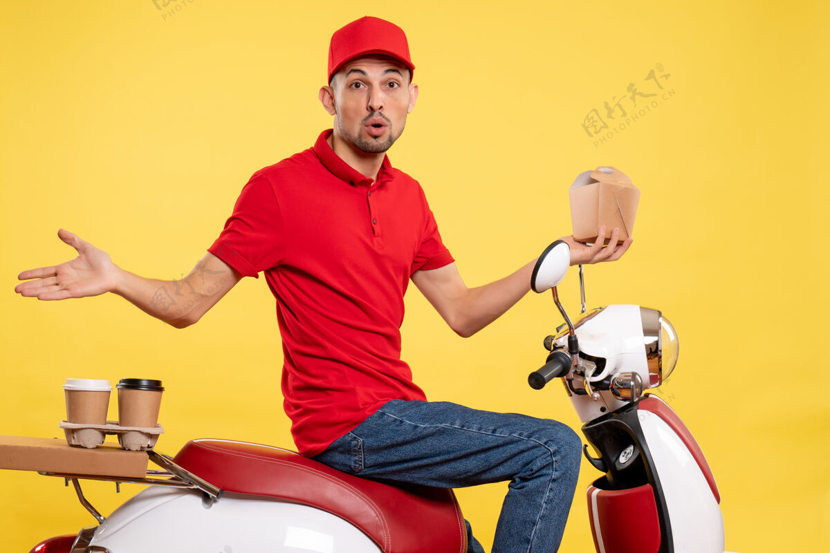 前方正面图身穿红色制服的年轻男性快递员 黄色背景上几乎没有送货食品视野黄色摩托车