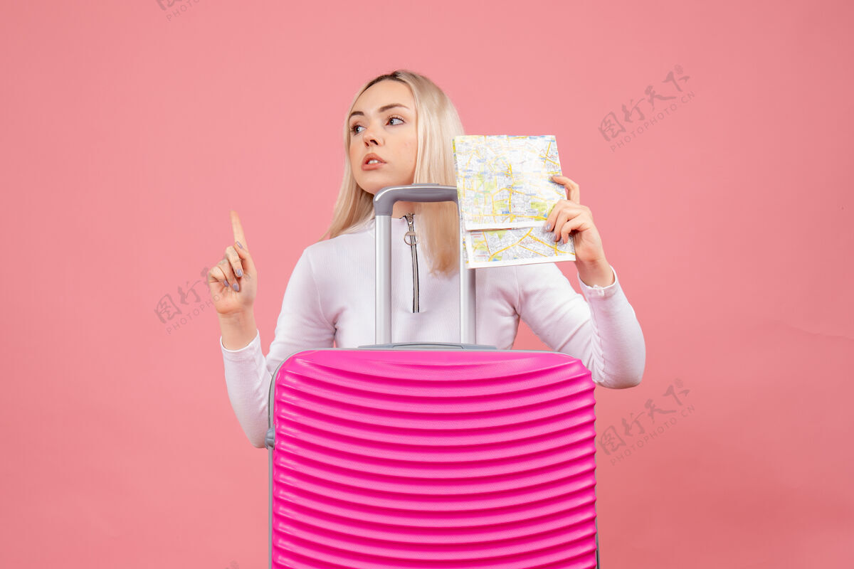 大人正面图：站在粉色手提箱后面的年轻女士拿着地图指着天花板手提箱地图拿着