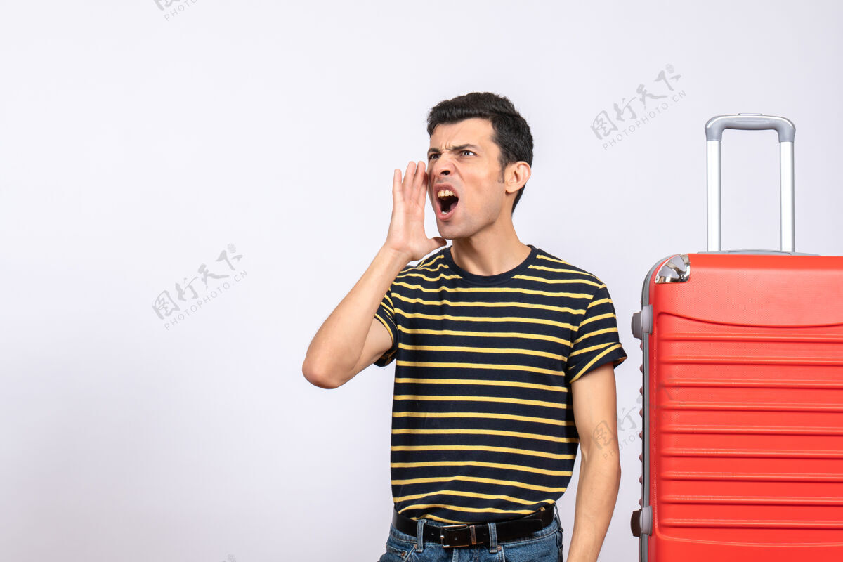 视图正面图：一个穿着条纹t恤和手提箱的年轻人在叫人电话前面电话