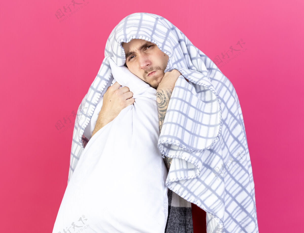 人一个穿着格子布的未出狱的年轻病人把枕头孤立地放在粉红色的墙上包裹人姿势