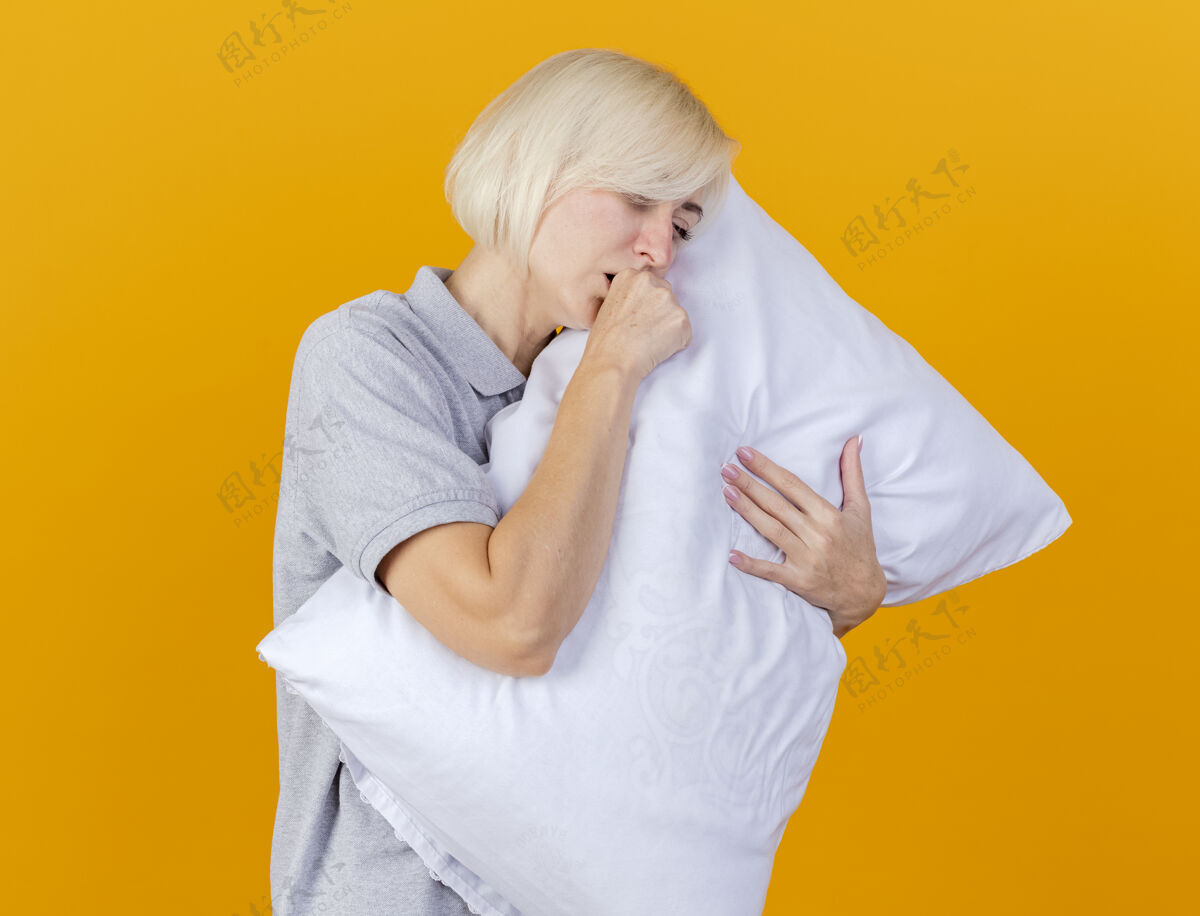 姿势咳嗽的年轻金发病女人抱着隔离在橙色墙上的枕头人表情拥抱