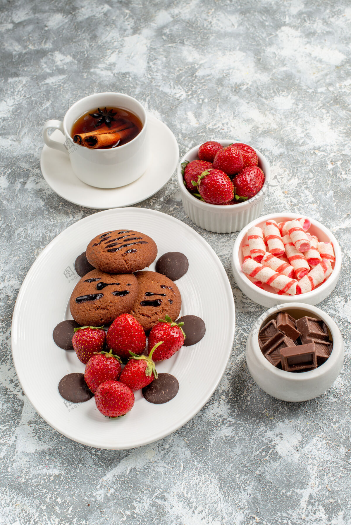 水果俯瞰饼干草莓和圆形巧克力放在椭圆形的盘子里一碗碗糖果草莓巧克力和肉桂茶放在灰白色的桌子上餐浆果巧克力
